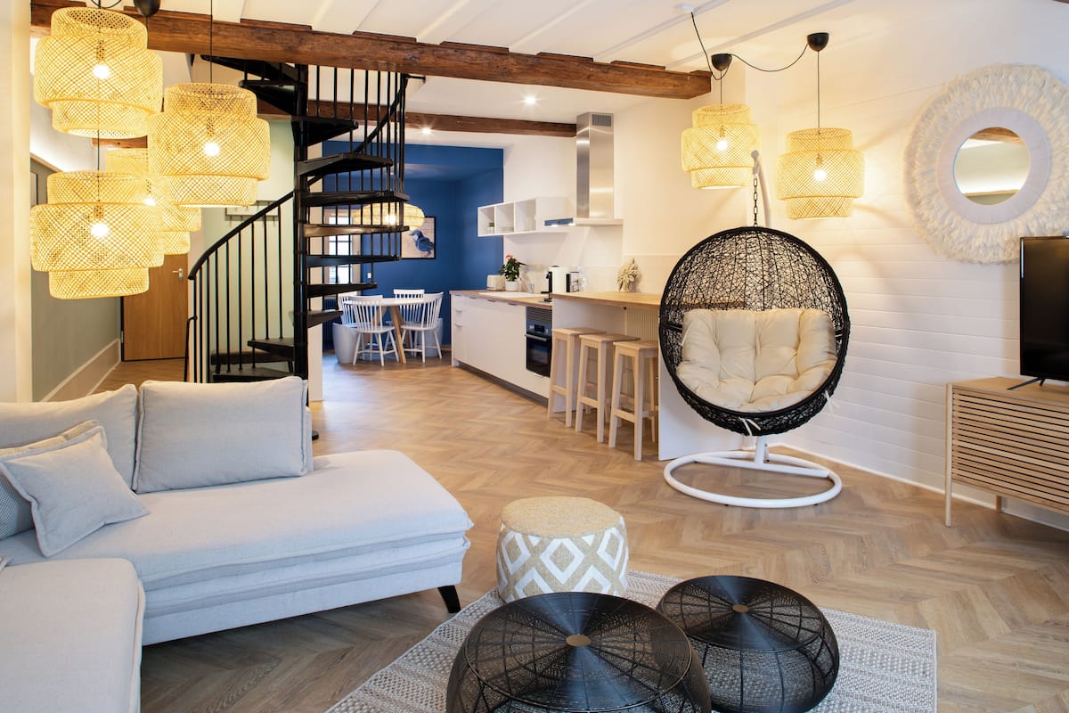 Un salon moderne avec un canapé, un pouf, des fauteuils suspendus et un escalier.