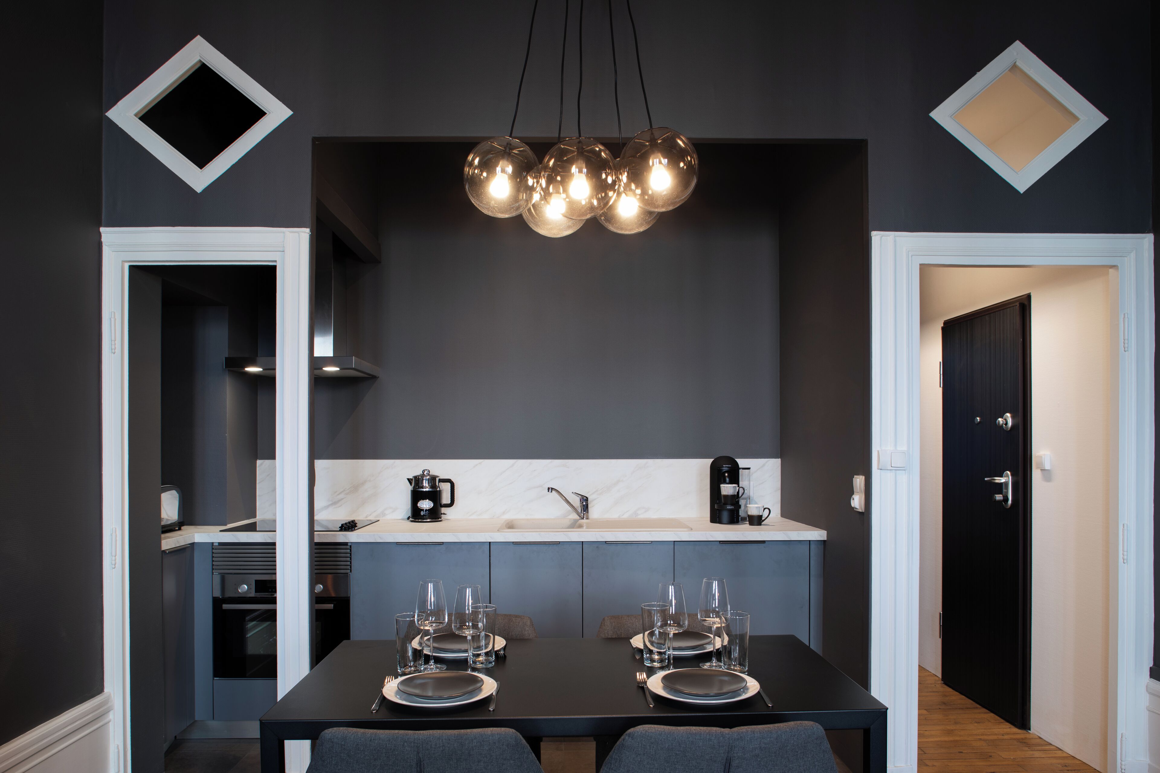 Een moderne keuken met een centraal eiland, een eetgedeelte met een tafel gedekt voor twee personen, en een zwarte deur die leidt naar een andere kamer.