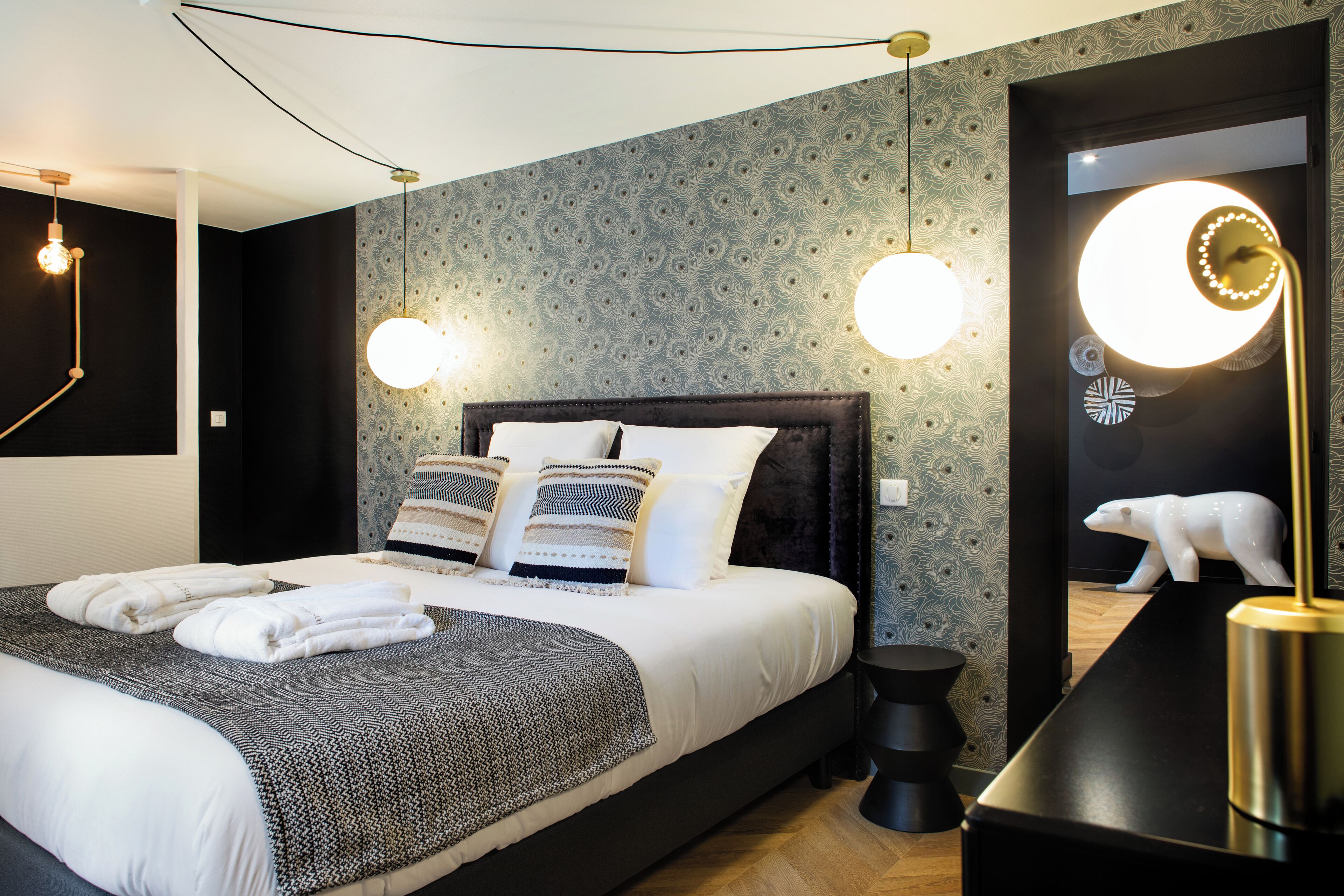 A modern bedroom with a large bed, two bedside lamps, a mirror with a polar bear decoration, and a black nightstand.