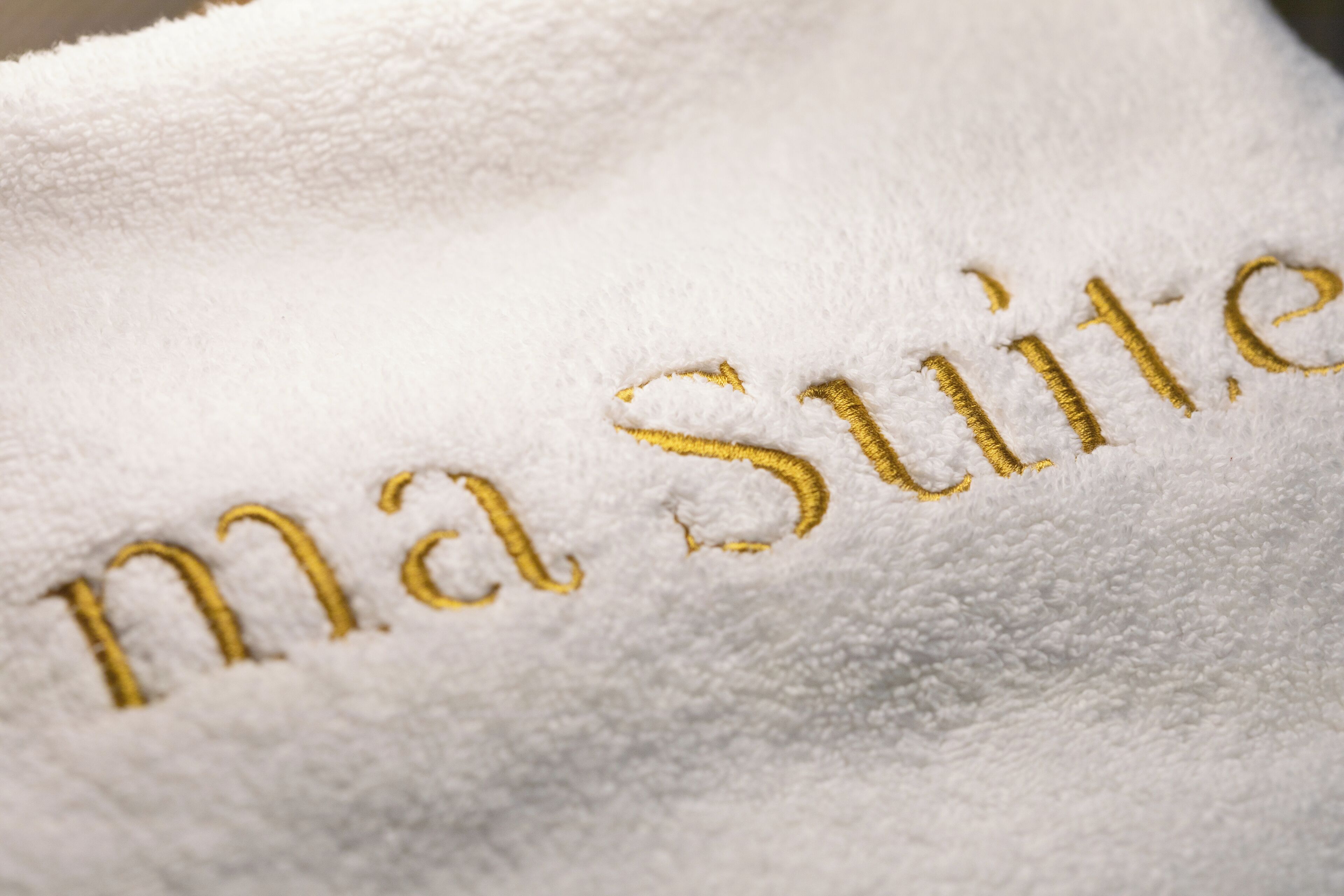 Toalla blanca con bordado dorado que dice 'ma Suite'.