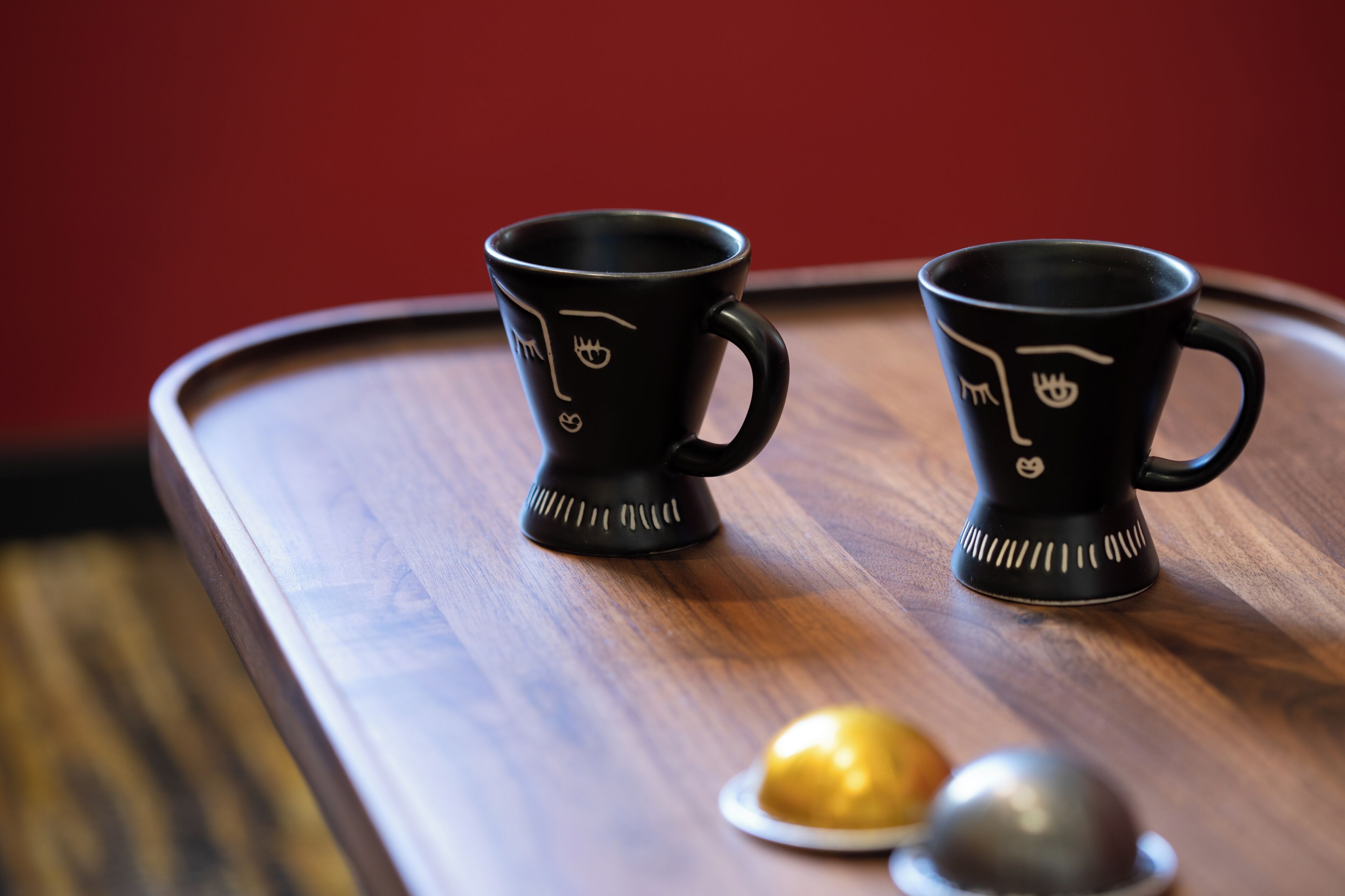 Two black cups with white designs on a wooden tray.