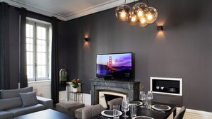 Un salon moderne avec une cheminée, une table à manger dressée pour quatre personnes, un canapé et un téléviseur fixé au-dessus de la cheminée.