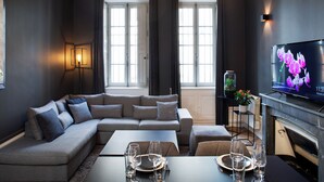 Un salon moderne avec un canapé d’angle, une table à manger pour quatre personnes, un téléviseur à écran plat et une cheminée.