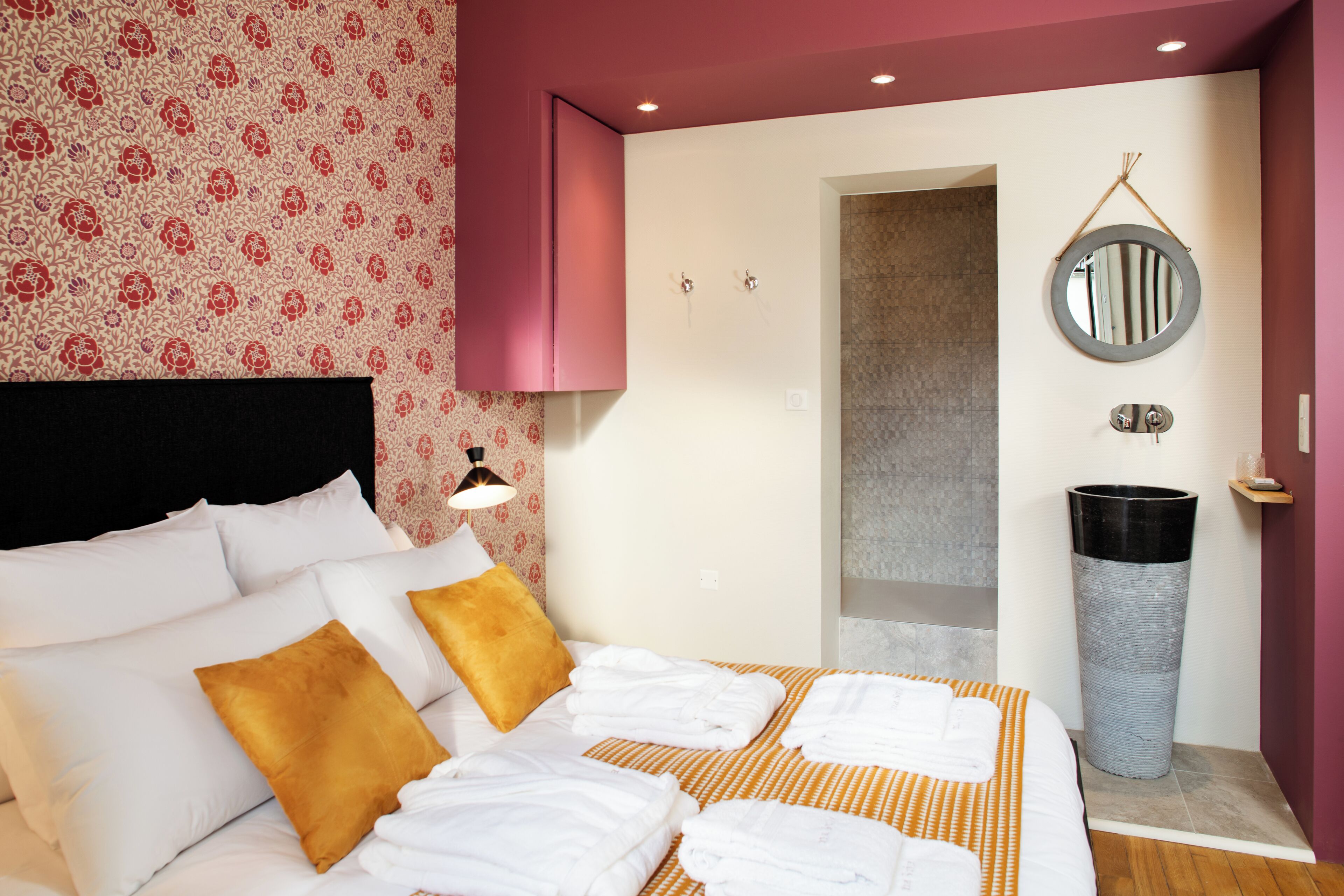 A hotel room with a bed, pillows, a bedside table, a mirror, and a trash can.