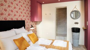 A hotel room with a bed, pillows, a bedside table, a mirror, and a trash can.