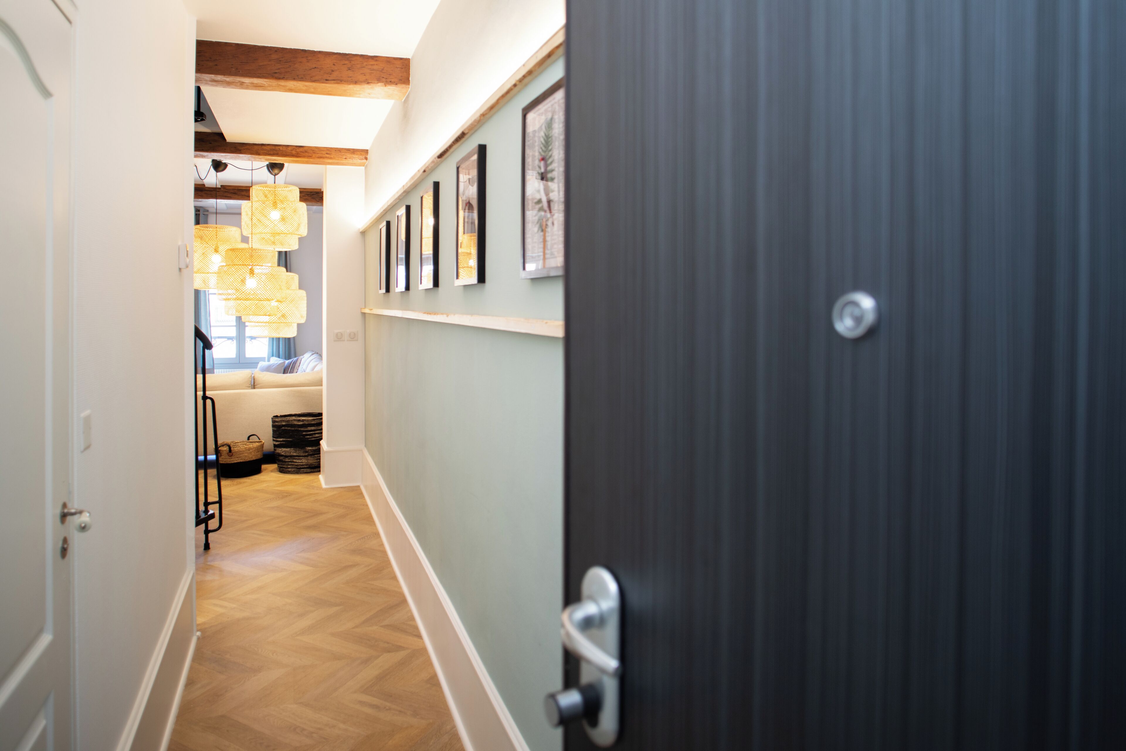 A hallway with wooden flooring, a dark door, and a wall with framed pictures.