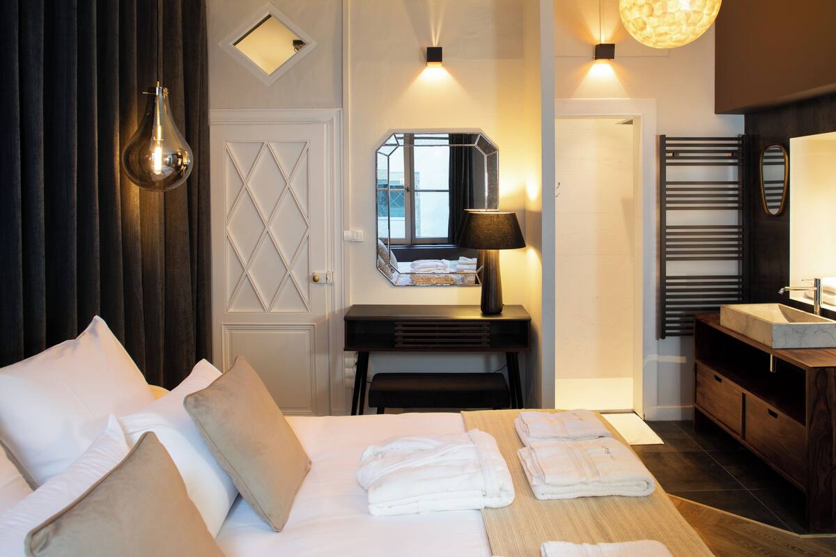 Une chambre d’hôtel comprenant un lit, une table de chevet et une salle de bain avec un lavabo et un miroir.