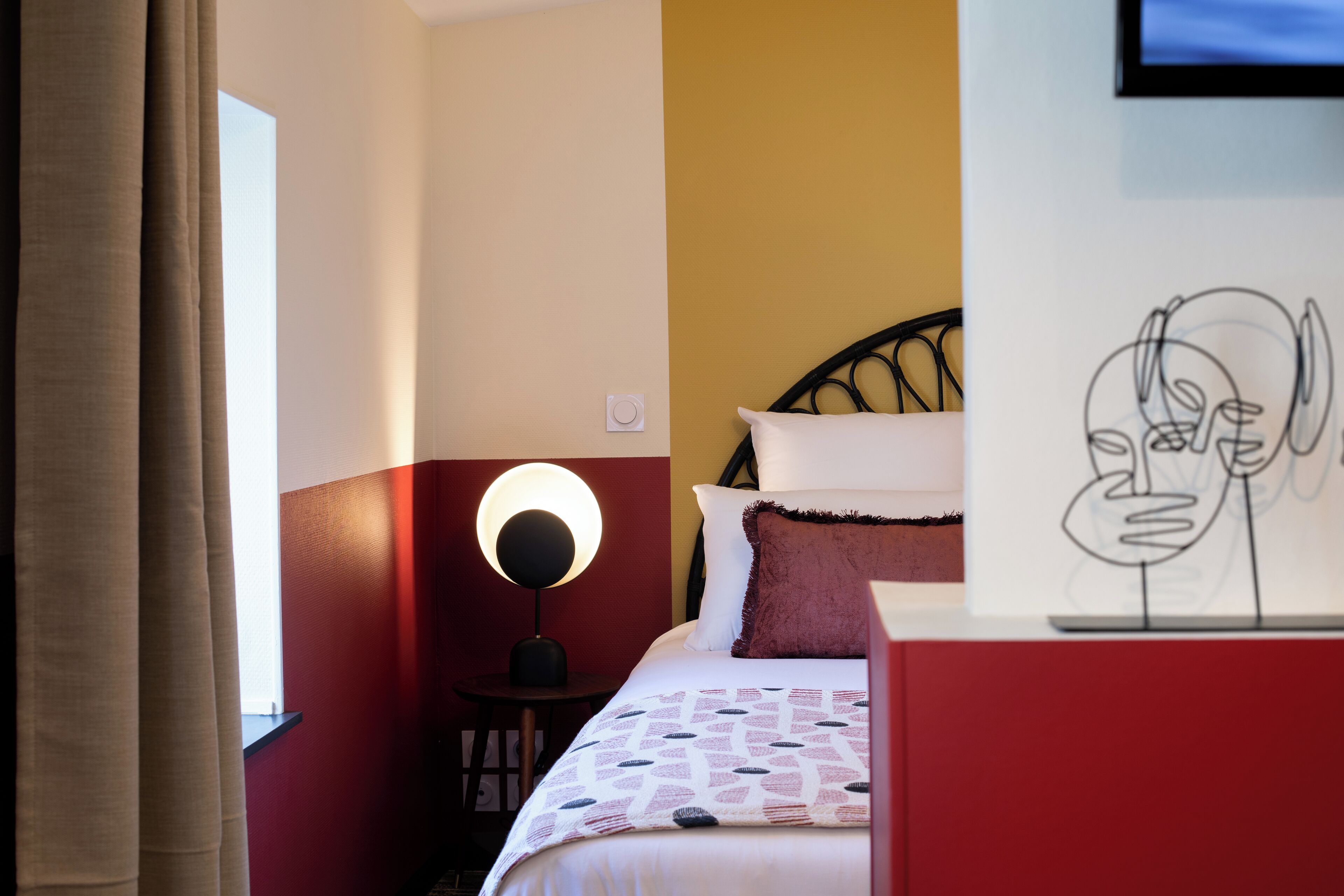 A hotel room with a bed, a bedside lamp, a wall clock, and a painting on the wall.