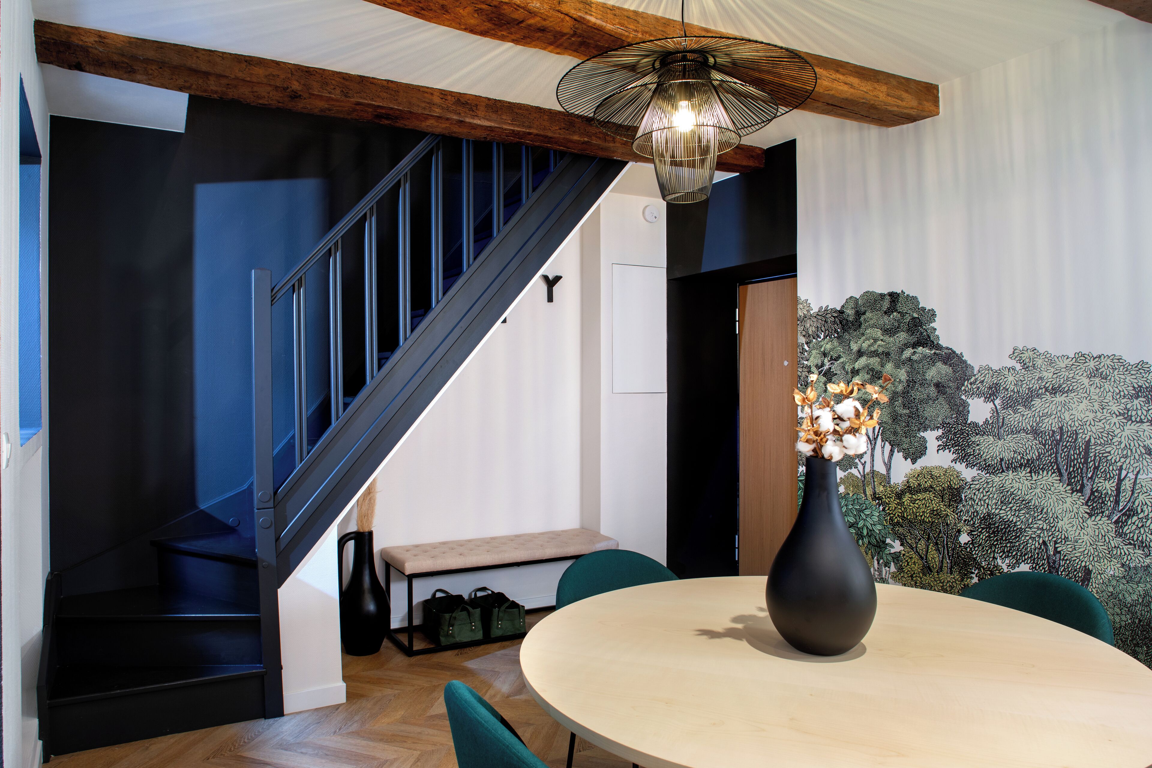 Un interior moderno con una escalera, una mesa redonda y un jarrón de flores.