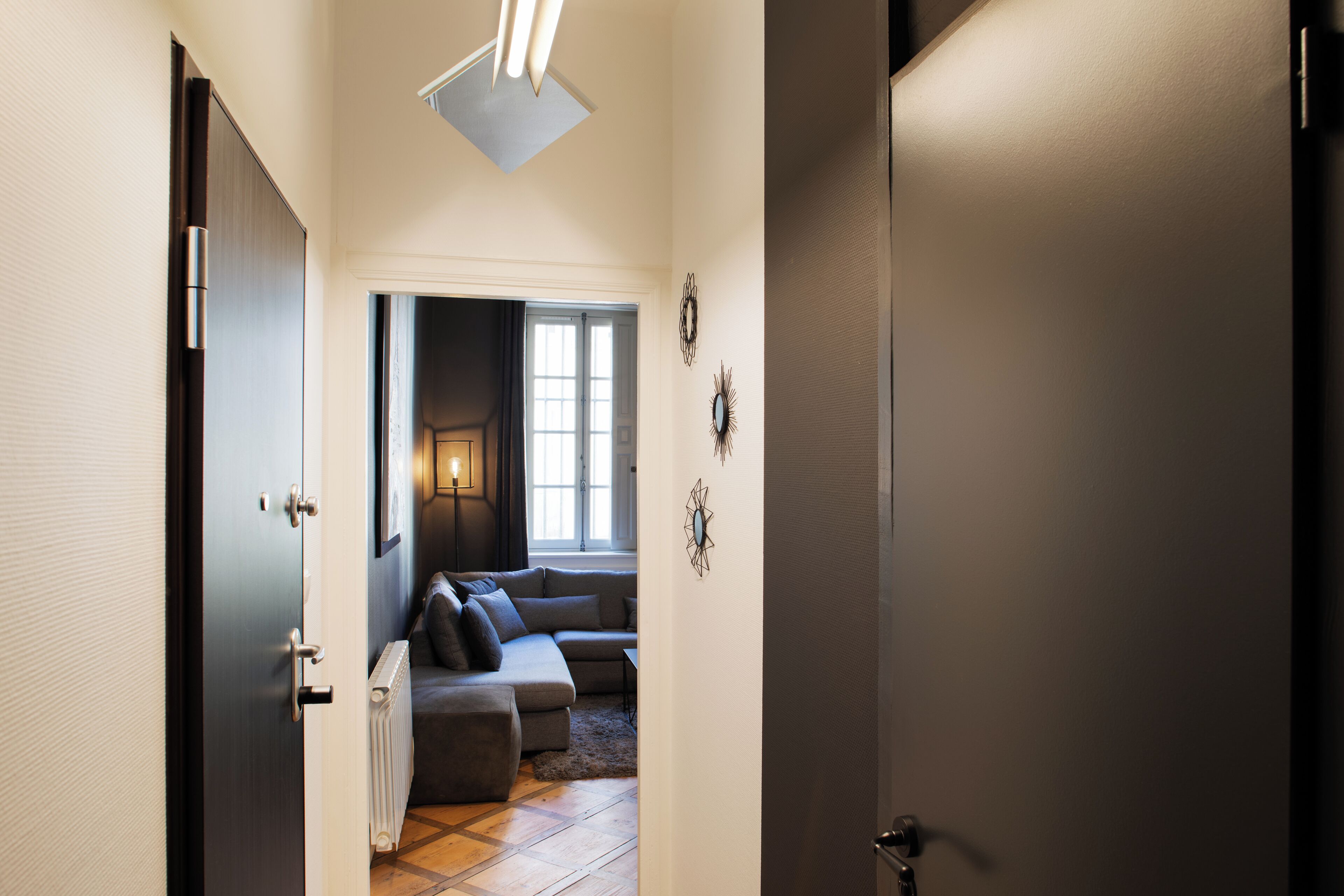 Un pasillo que lleva a una sala de estar con sofá, un radiador y decoración en las paredes.