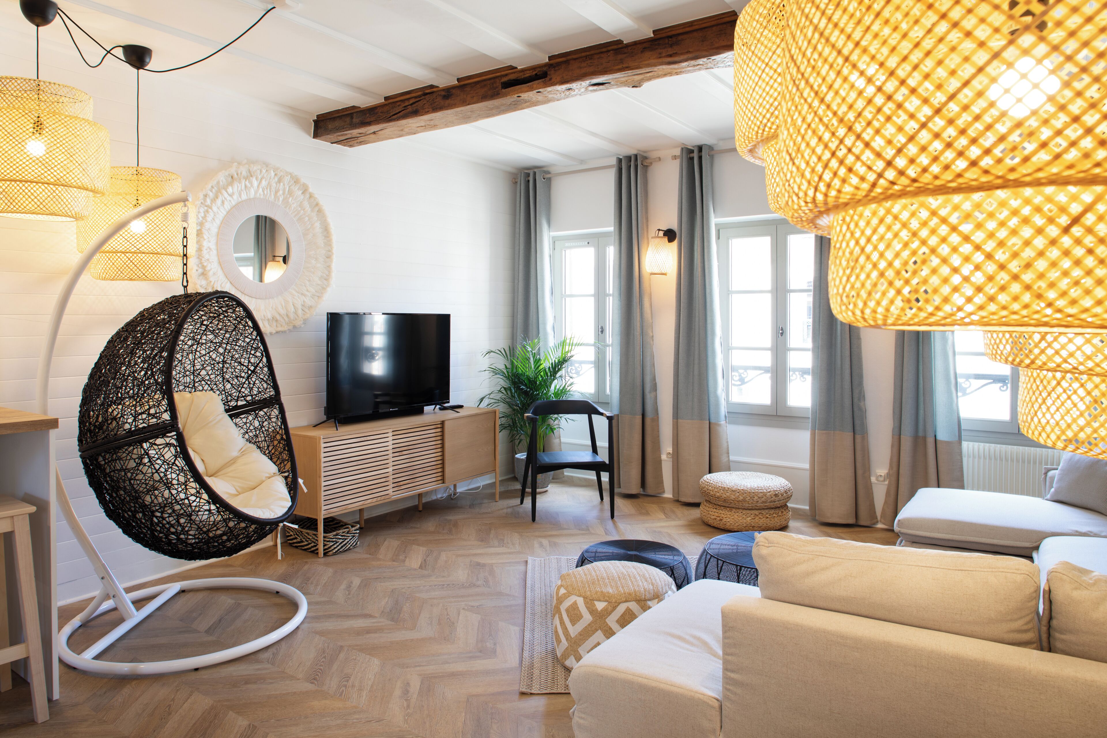 A modern living room with a hanging chair, a sofa, a television, and a large window with curtains.