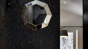 Un bagno con uno specchio esagonale, un lavandino nero di grandi dimensioni e un divano rosso nella stanza adiacente.