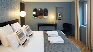 A hotel room with a neatly made bed, a desk with a lamp, a chair, and a large window with curtains.