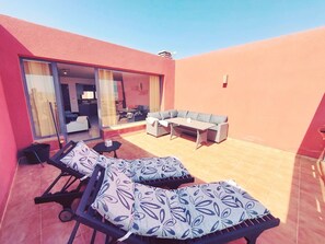 Eine sonnendurchflutete Terrassenanlage mit zwei Liegestühlen, einem Sofa und einem Esstisch.