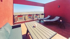 A balcony with two lounge chairs, a small table, and a view of distant mountains. - Casa Bella Vista - pool - WiFi - Table tennis  (Antigua)