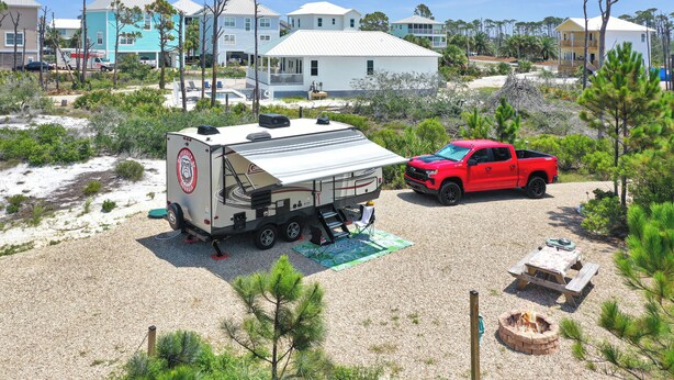 A campsite with a recreational vehicle, a red pickup truck, and a fire pit.