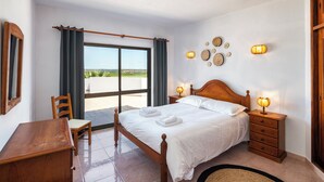 A bedroom with a bed, wooden nightstands, a desk, a chair, a large window with curtains, and wall-mounted lights. - Villa Luz 21, Ruime Villa met Privé Zwembad (Silves)