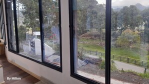 Habitación de hotel con ventanas amplias que ofrecen vista a un área ajardinada con árboles y una carretera.