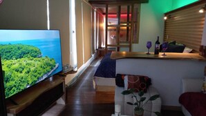 Una sala de estar moderna con un televisor de pantalla plana grande, una mesa de centro de madera, un sofá y una pequeña zona de bar con una botella de vino y una copa.
