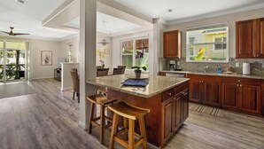 A spacious kitchen with a large island, wooden cabinets, and a view to the outdoors. - Nihilani at Princeville 28B By Parrish Kauai (Princeville)
