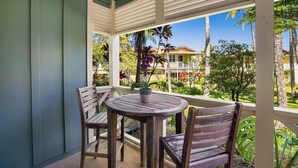 A covered outdoor seating area with a table and two chairs, overlooking a residential neighborhood with houses and lush greenery. - Nihilani at Princeville 28B By Parrish Kauai (Princeville)