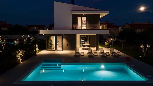 Ein modernes, zweistöckiges Haus mit Swimmingpool, Außenbereich zum Sitzen und einem einsehbaren Innenraum mit Essbereich.