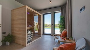 Ein modernes Zimmer mit einem Holzkabinett, einem Esstisch mit Stühlen, einer Kühlpflanze und Blick auf ein Schwimmbad durch große Glasüren.