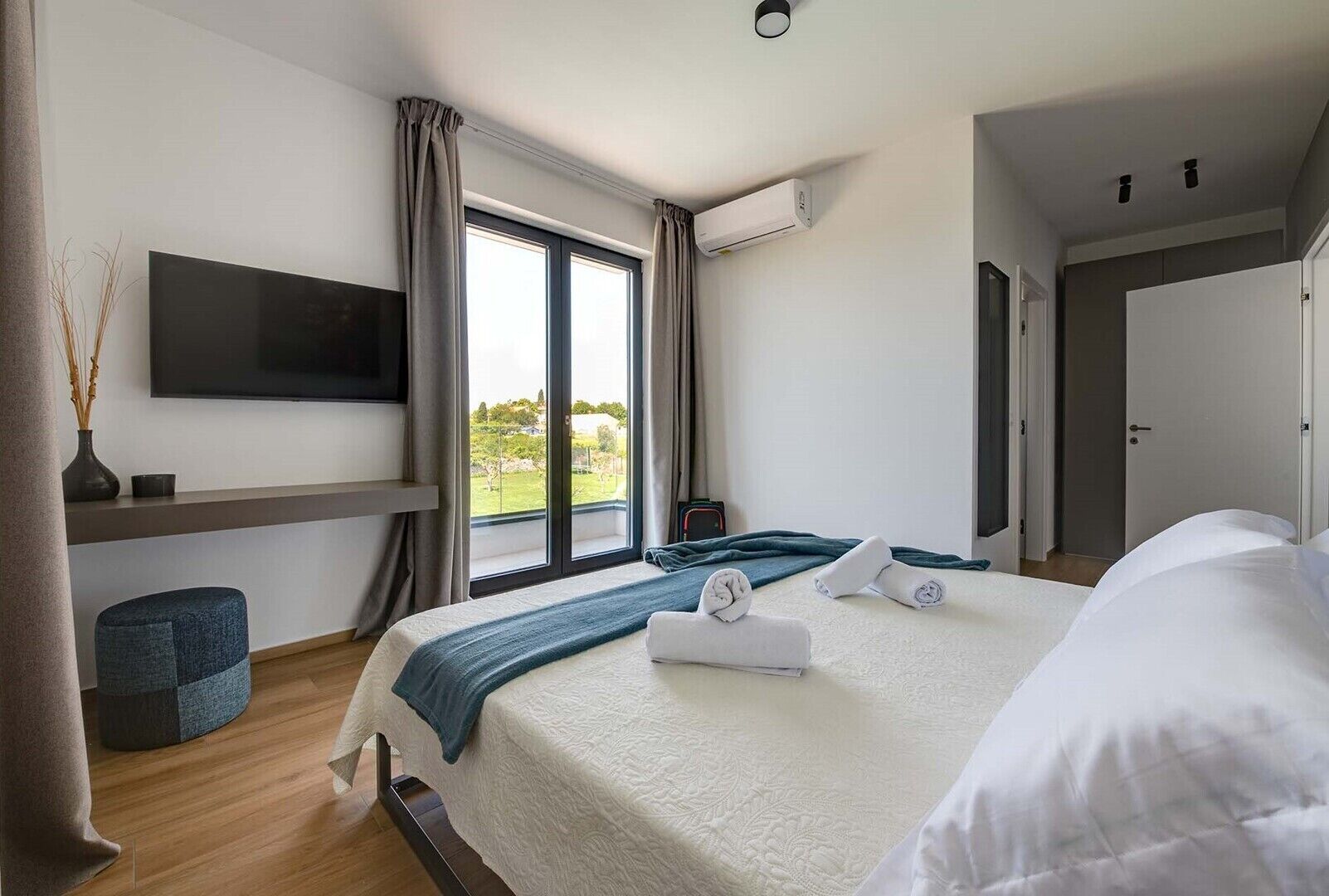 Una camera d'albergo moderna con un letto grande, una TV a parete e una finestra con tende.