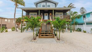 A two-story house with a front porch, wooden steps, and palm trees. - The Poop Deck: *Pet-friendly *Canalfront *Heated Pool *Sleeps 8 (Anna Maria)
