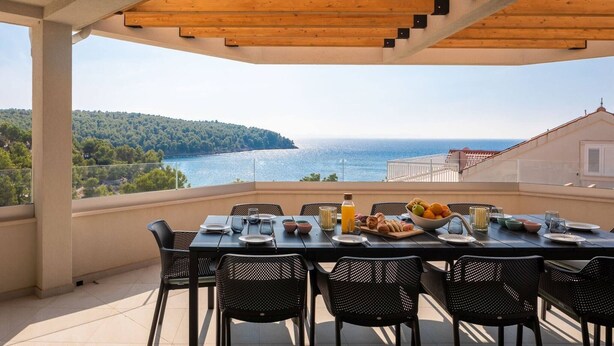 A balcony with a table set for breakfast, overlooking a scenic view of the sea and a forested hill. - Luxury Villa Leisure Seaside Brac with Pool (Milna)