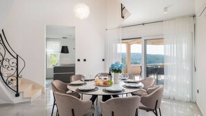 A dining area with a round table set for six, a vase of flowers, and a view through large windows. - Luxury Villa Leisure Seaside Brac with Pool (Milna)