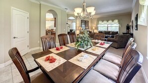 A dining area with a long table, chairs, and a chandelier. There is a kitchen in the background and a living area with a couch and a plant. - 4 Bed 4 Bath With Private Pool/spa 4 Bedroom Home by RedAwning (Davenport)