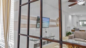 A modern living room with a large flat-screen TV mounted on the wall, a ceiling fan, and a wooden coffee table. - Large 7 Bed In Solterra Pool, Spa Near Disney 7 Bedroom Home by RedAwning (Davenport)