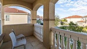 A balcony with a white chair, a table, and a view of neighboring houses. - Large 7 Bed In Solterra Pool, Spa Near Disney 7 Bedroom Home by RedAwning (Davenport)