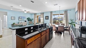 A modern kitchen with a black granite countertop, wooden cabinets, and a dining area with a table and chairs. - Large 7 Bed In Solterra Pool, Spa Near Disney 7 Bedroom Home by RedAwning (Davenport)