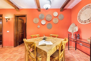 Un comedor con una mesa y sillas de madera, rodeado por una pared naranja vibrante decorada con tapices de pared.
