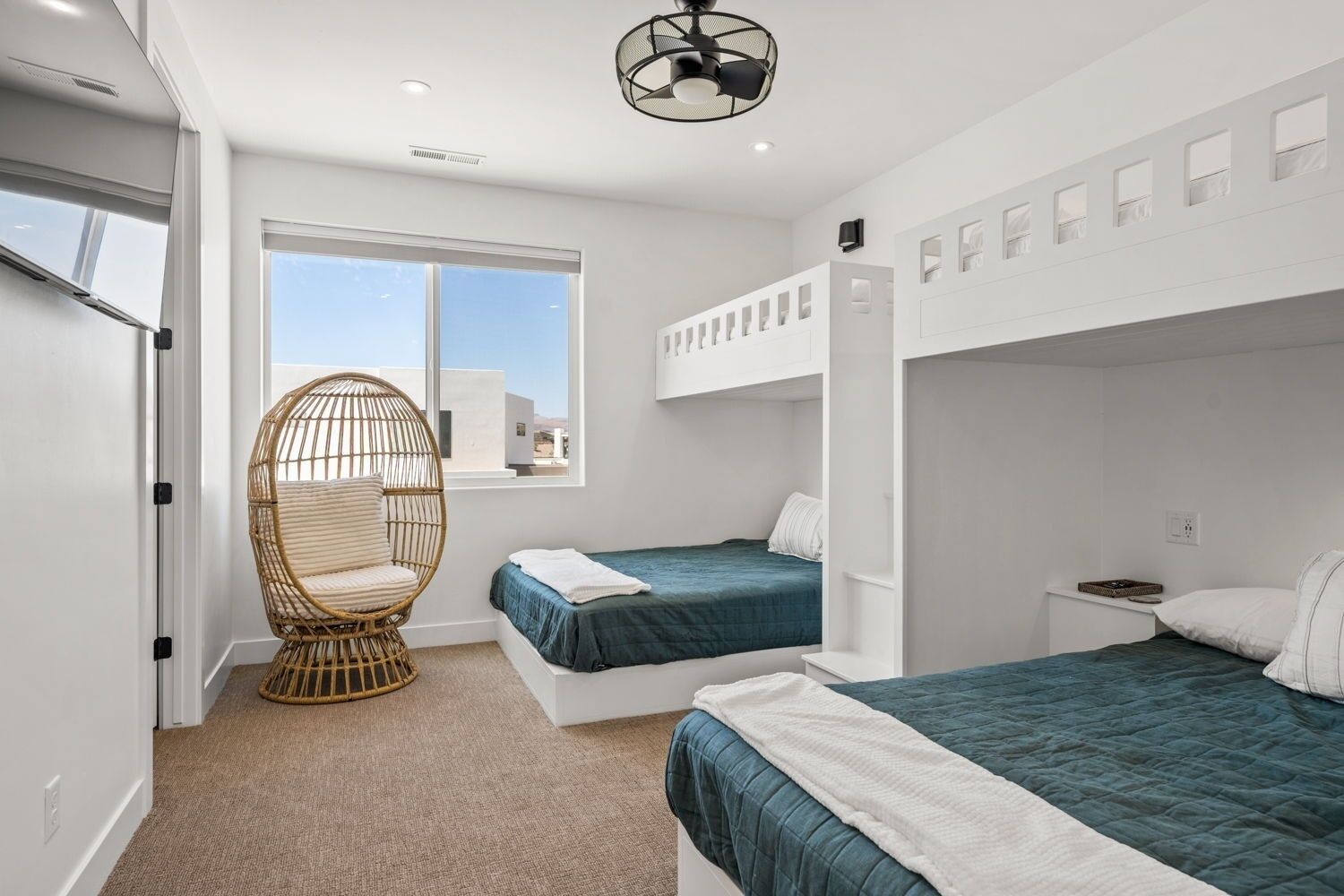 A modern bedroom with bunk beds, a rattan chair, and a large window offering a view.