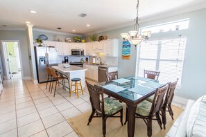 A modern kitchen with white cabinets, a stainless steel refrigerator, and a dining area with a glass table and wooden chairs.