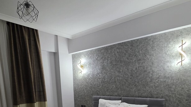 Un dormitorio moderno con una cama grande, cabecera con iluminación integrada, una mesita de noche y un aplique de techo.