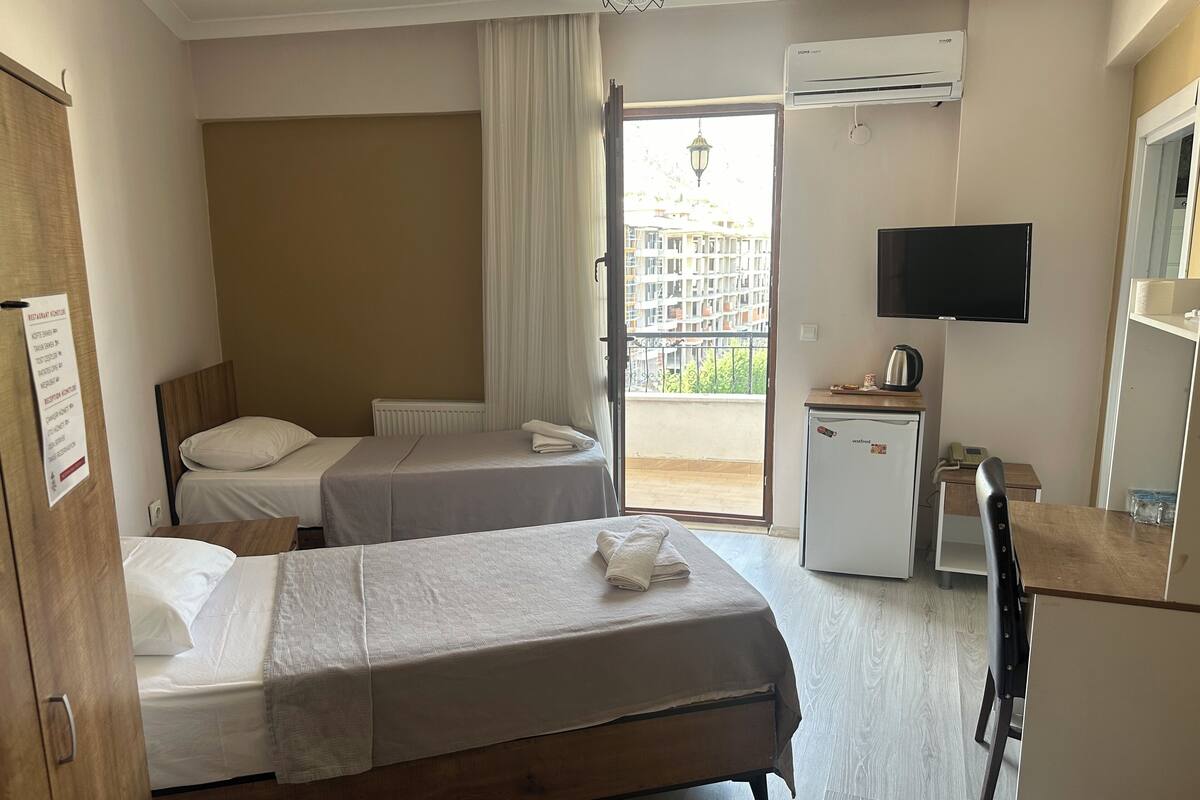 A hotel room with two beds, a desk with a television, a small refrigerator, and a view of the outside balcony.