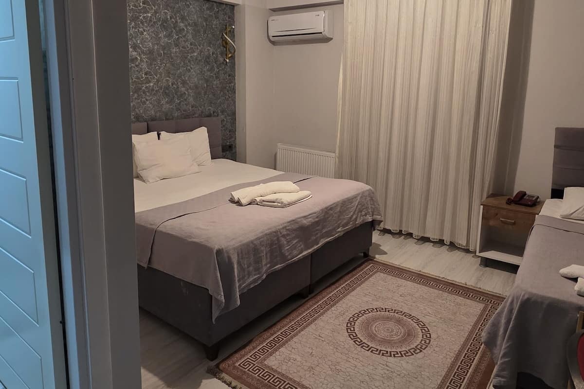 A modern bedroom with a large bed, a bedside table, a nightstand, a wall-mounted air conditioner, and a ceiling light fixture.