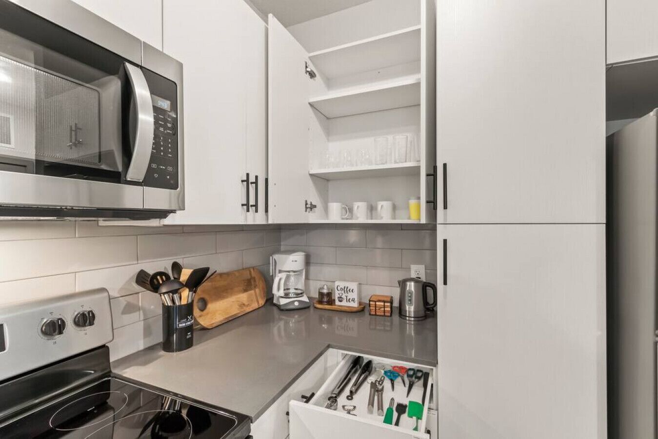 Een moderne keuken met witte kasten, een magnetron, een koffiezetapparaat en diverse keukengerei.