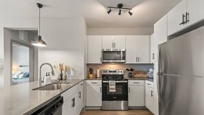 A modern kitchen with white cabinets, stainless steel appliances, and a wooden floor.
