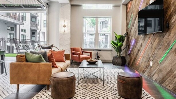 Un área de descanso moderna con un sofá, sillones, una mesa de centro y un televisor montado en la pared.
