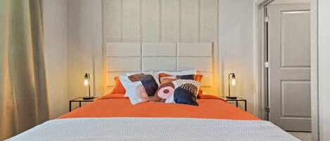 A neatly made bed with an orange bedspread and white bedding, flanked by two bedside lamps.