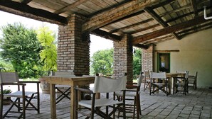 Eine Terrasse im Freien mit rustikalen Holztischen und -stühlen, Ziegelpfeilern und einem überdachten Dach.