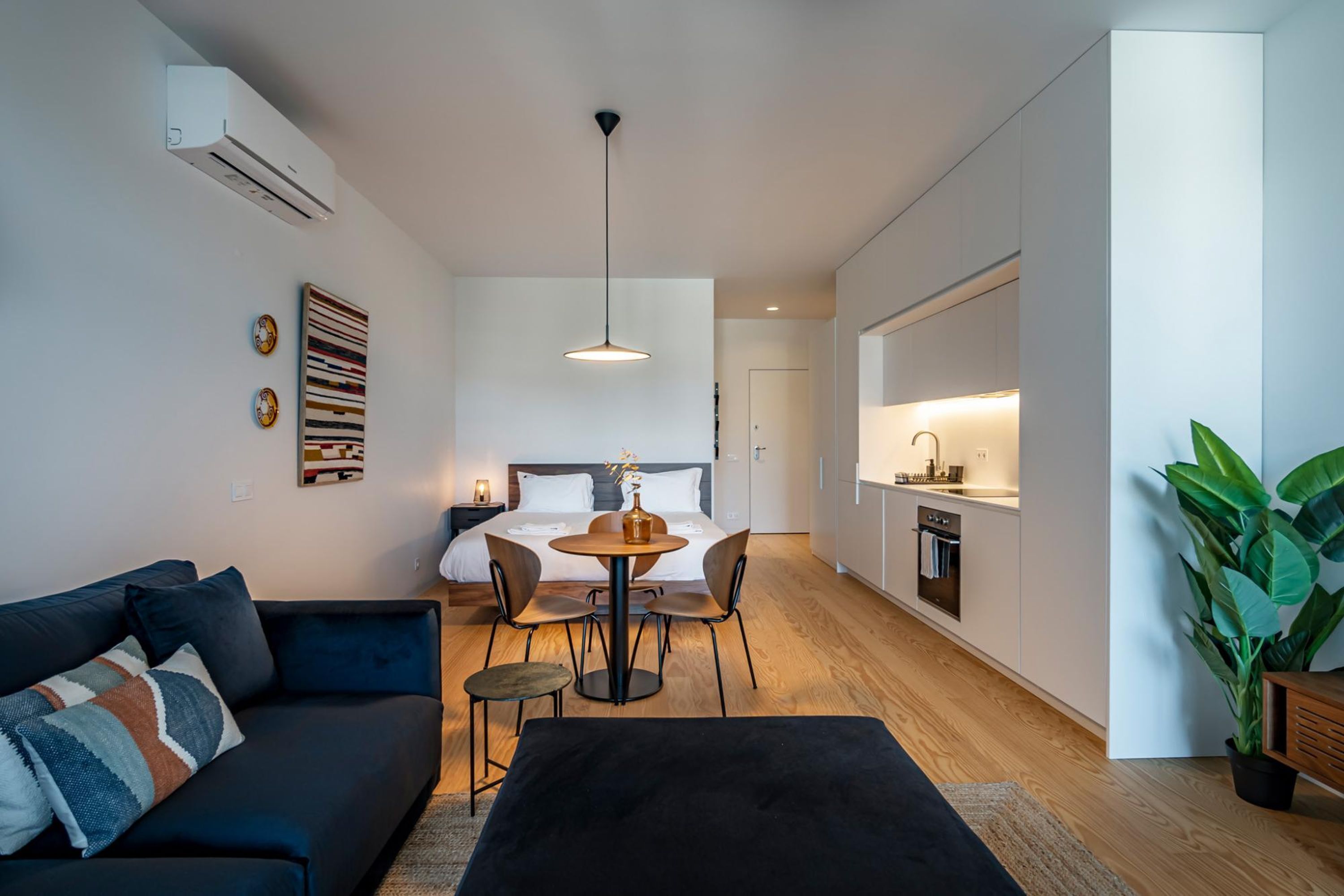 A modern, compact living space with a sofa, dining table, and chairs, a bed, and a kitchen area.