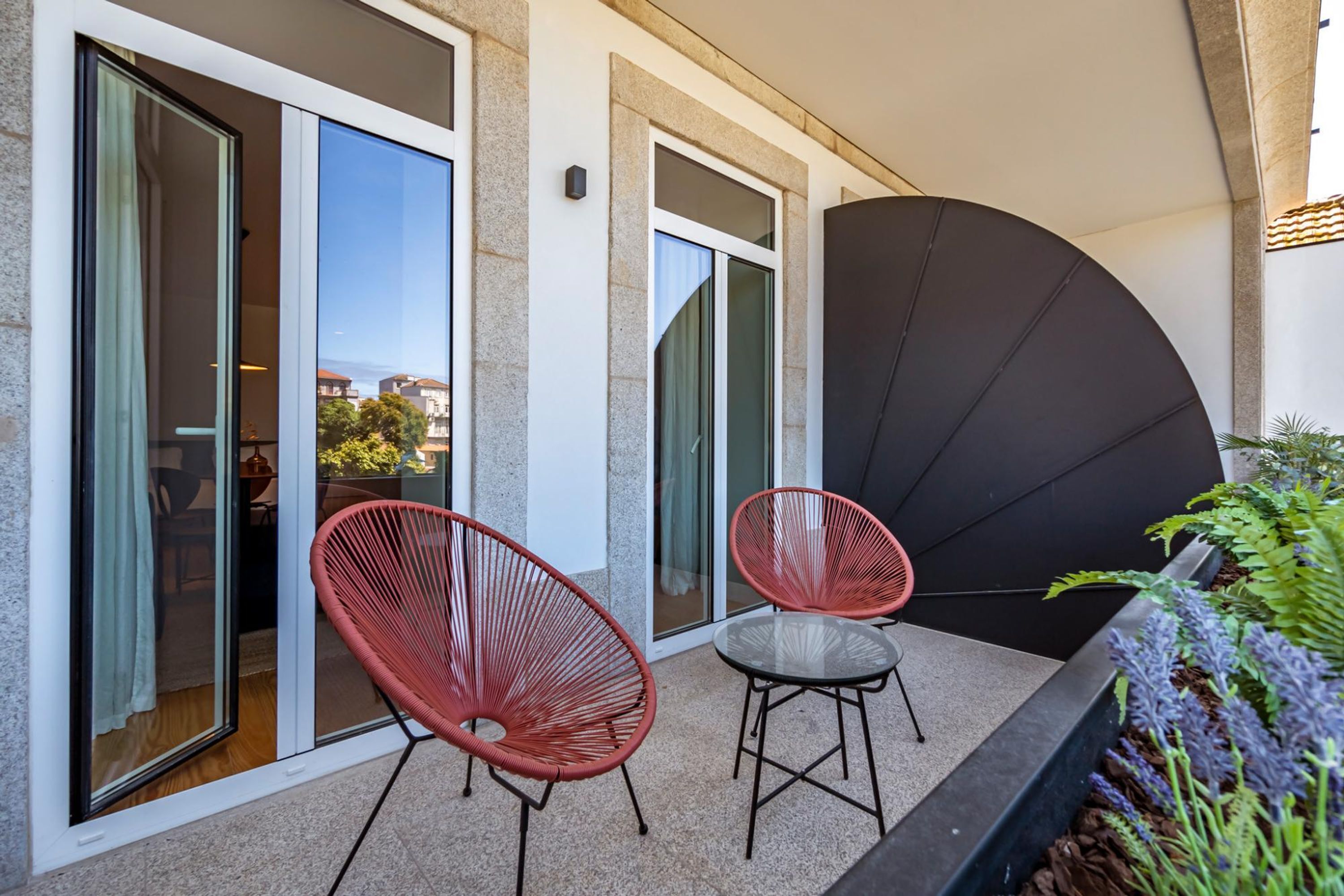 A balcony with two red chairs, a glass table, and a black umbrella.