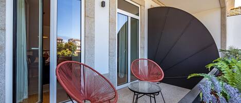 A balcony with two red chairs, a glass table, and a black umbrella.