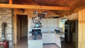 Una cocina con una isla central, vigas de madera en el techo, pared de piedra y estufa roja.